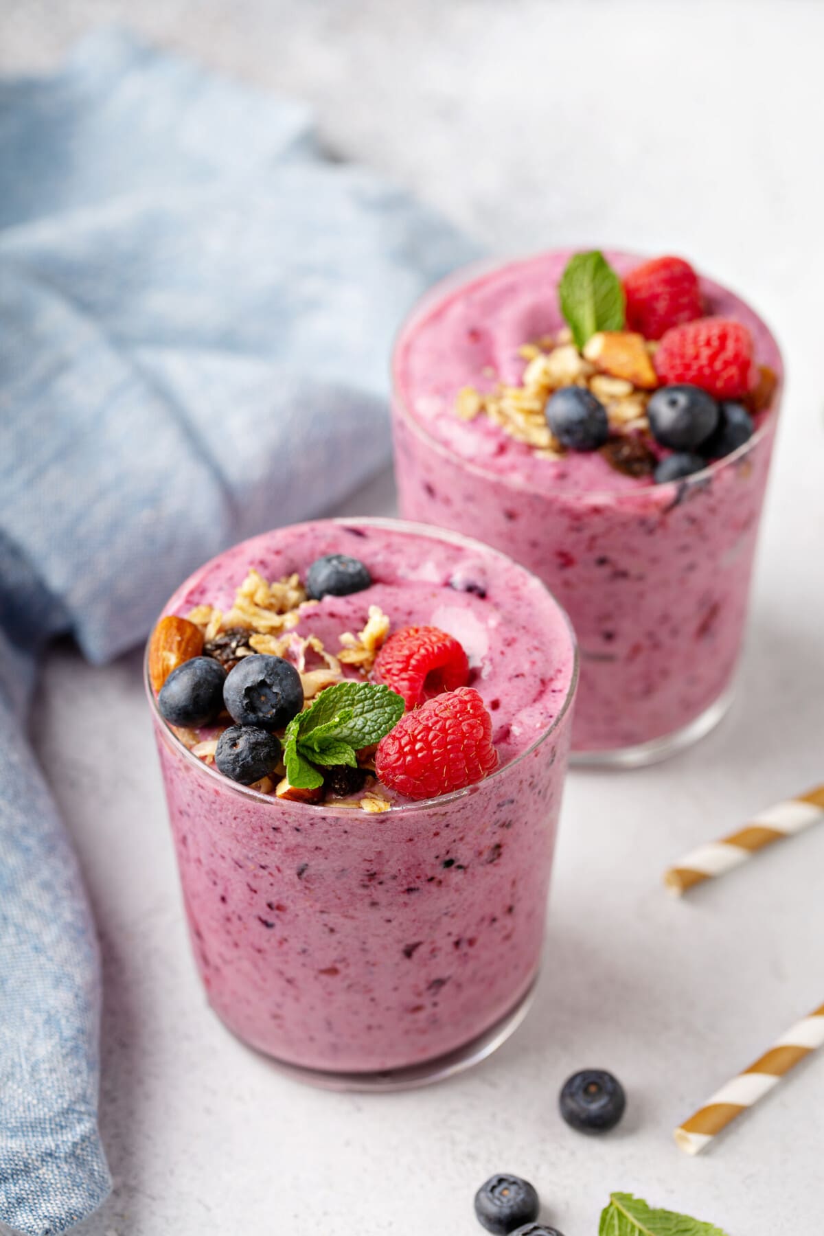 two mixed berry smoothies, topped with crushed nuts, fresh berries, and mint