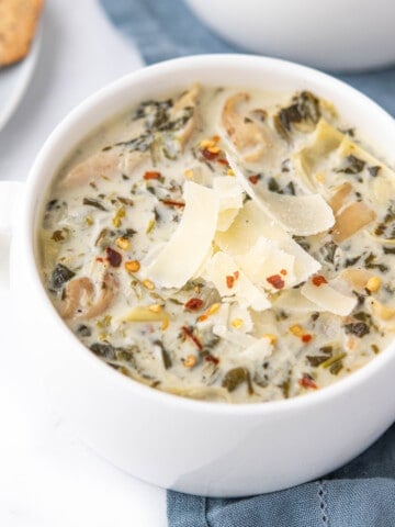 Bowl of spinach and artichoke soup in a white bowl, topped with shaved parmesan cheese and red pepper flakes