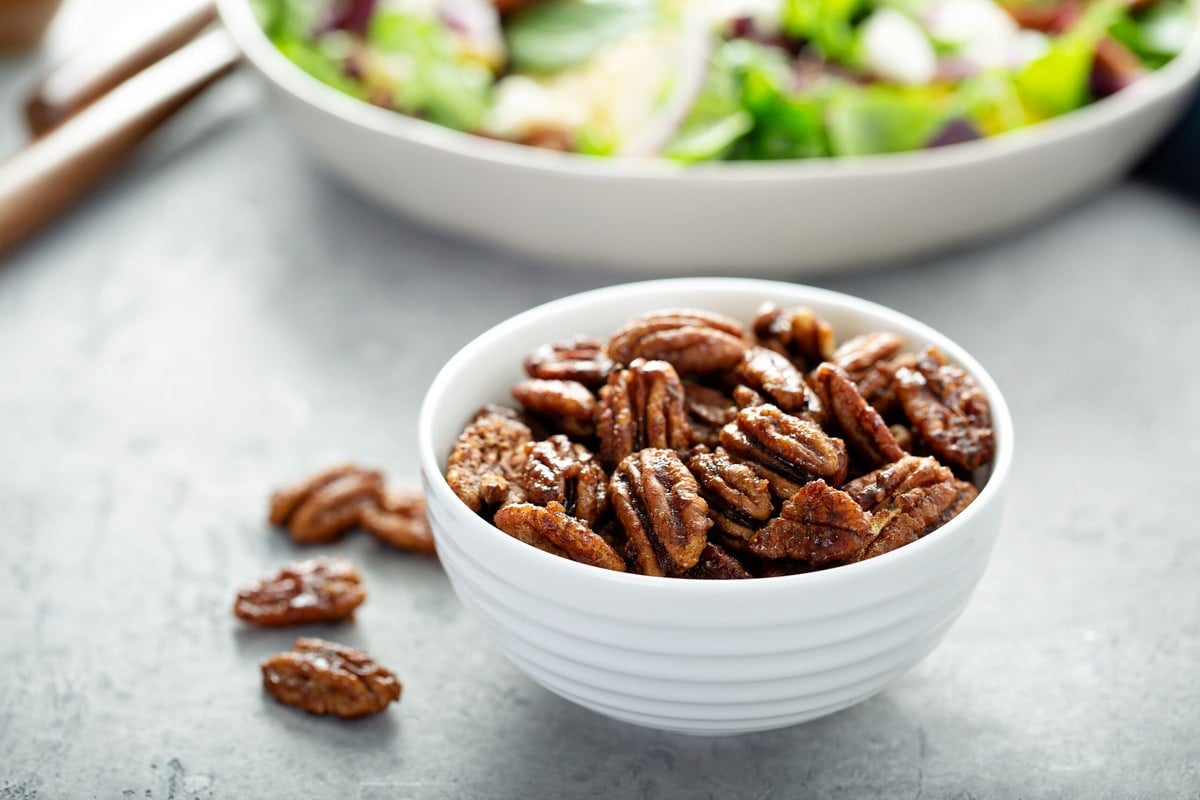 low carb candied pecans in a white bowl, with a salad in the background 