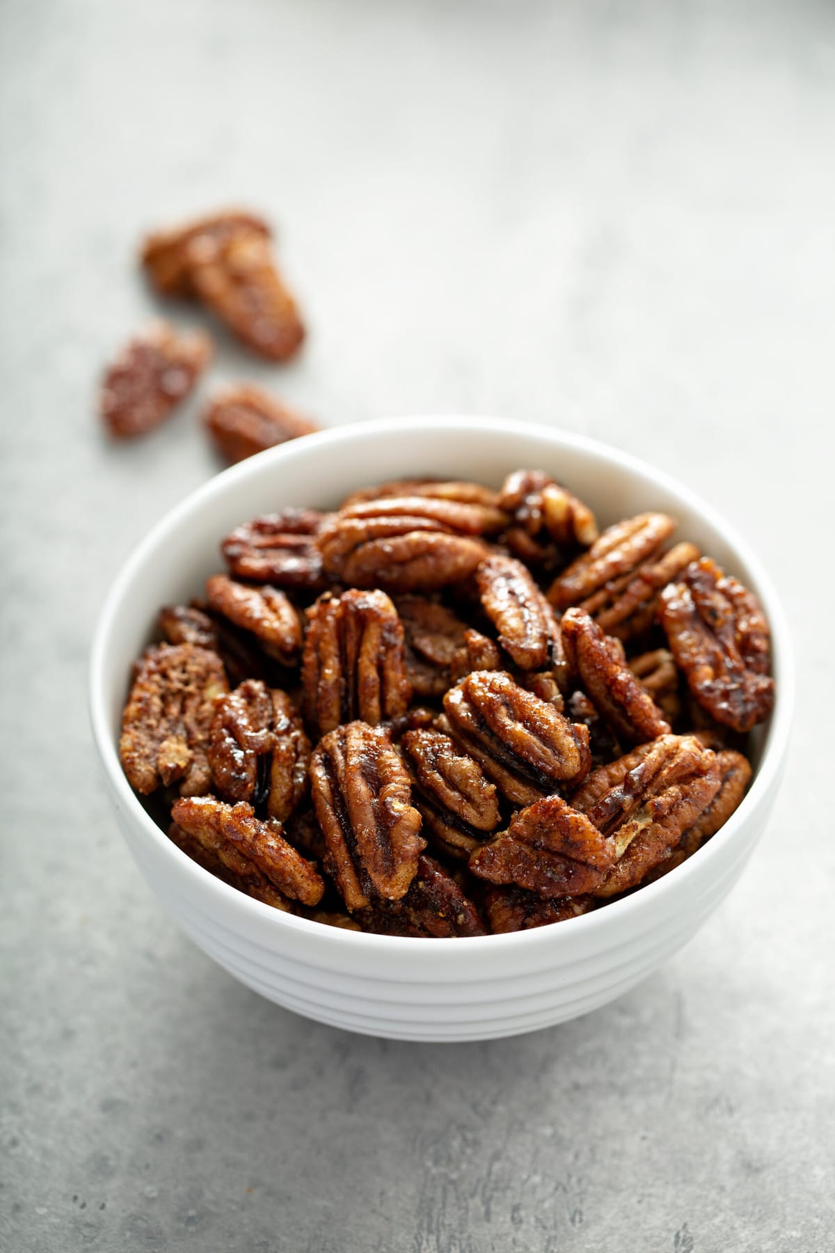 candied pecans in a white bowl on a concrete surface