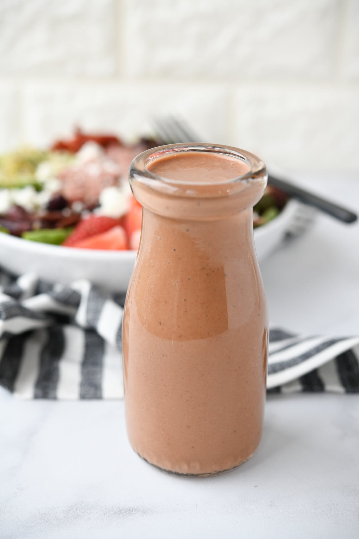 bottle of strawberry balsamic salad dressing with a salad in the background