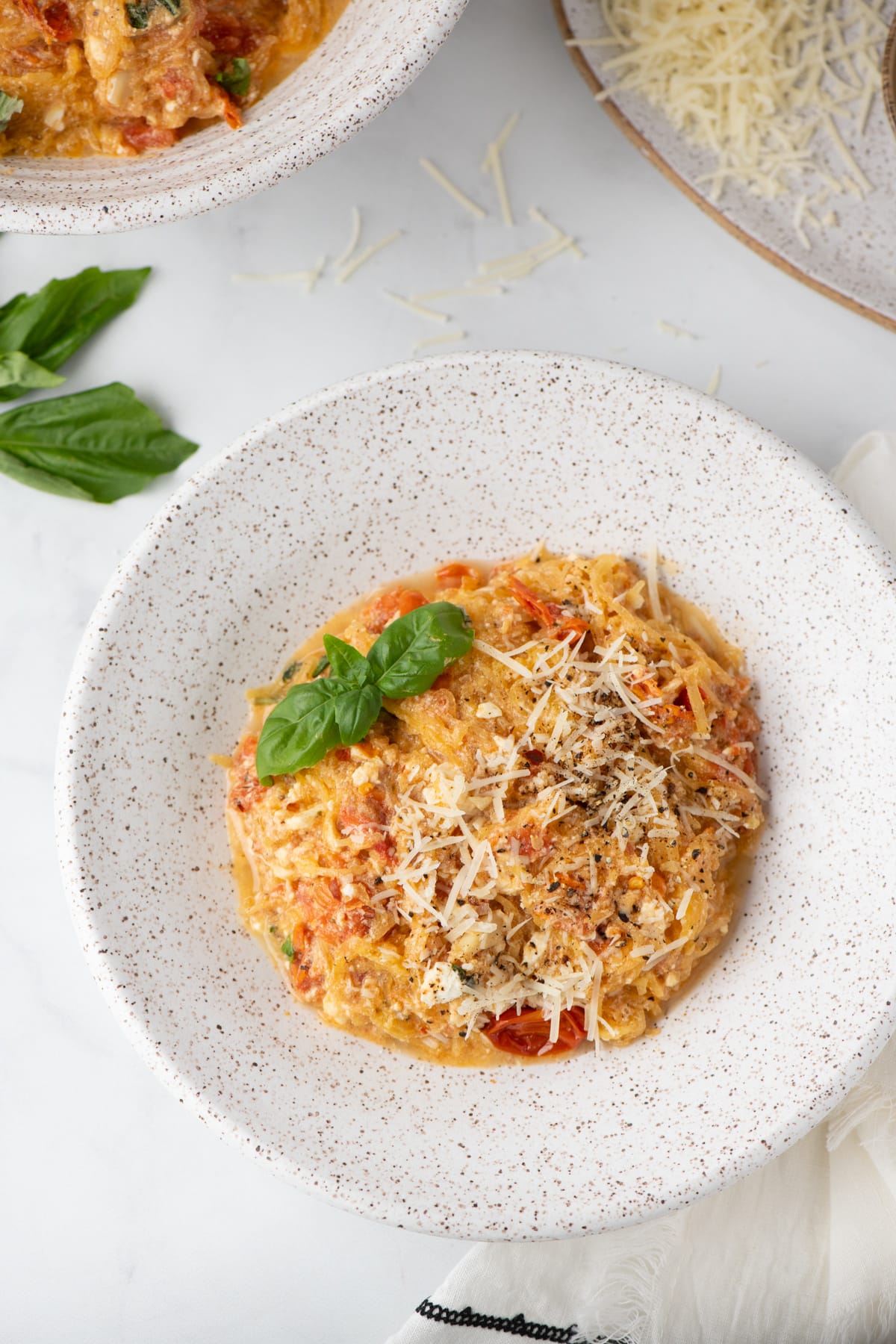 An overhead shot of a specked pottery bowl filled with a low carb baked feta pasta with tomatoes, basil and topped with cheese