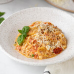 A specked pottery bowl filled with a low carb baked feta pasta with tomatoes, basil and topped with cheese