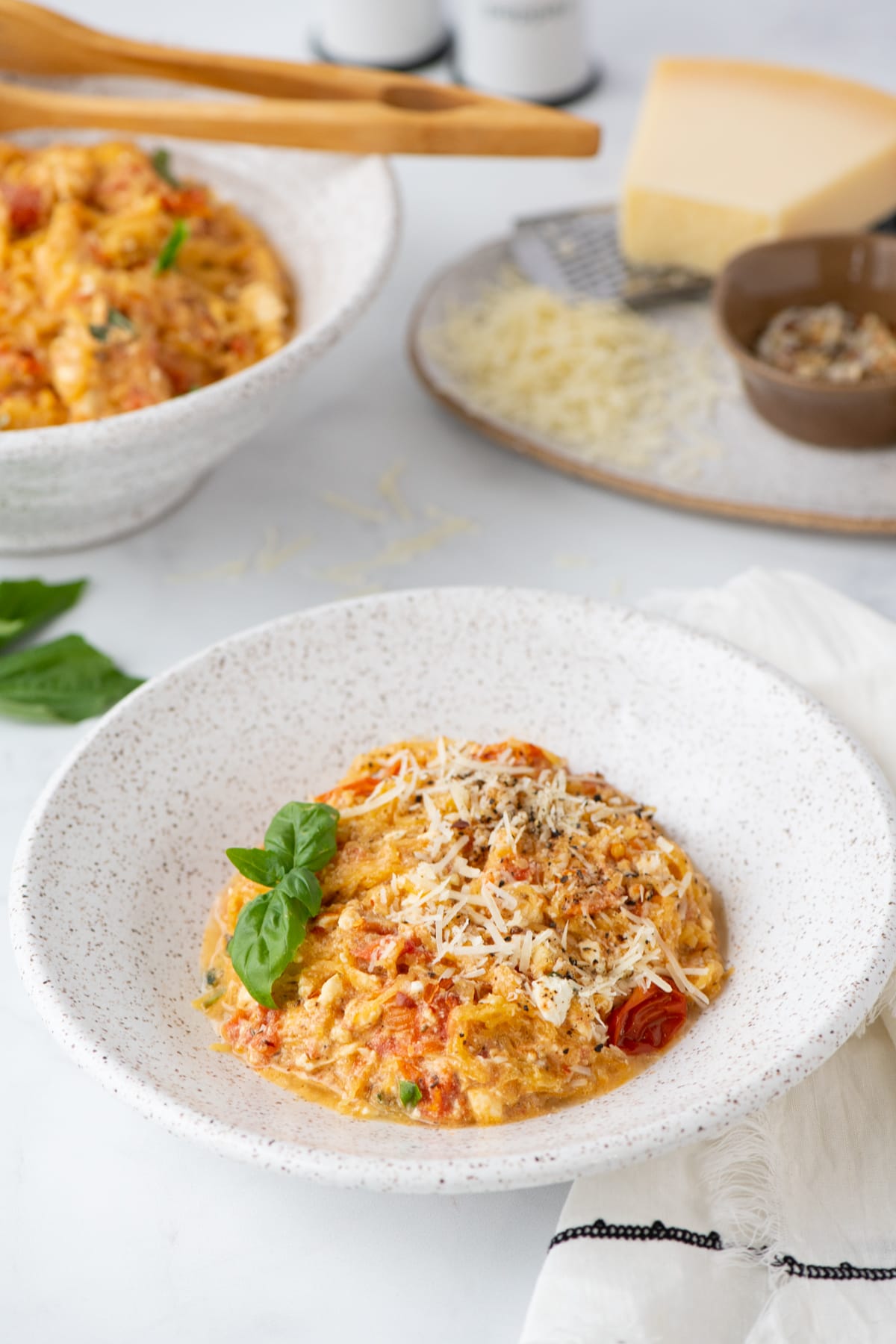 A specked pottery bowl filled with a low carb baked feta pasta with tomatoes, basil and topped with cheese