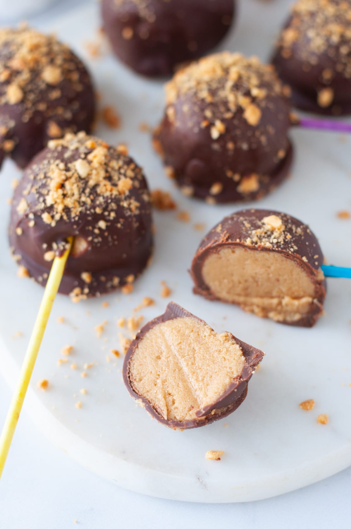 Chocolate Peanut Butter Pops coated  in crushed peanuts and lined on a parchment paper lined baking sheet.