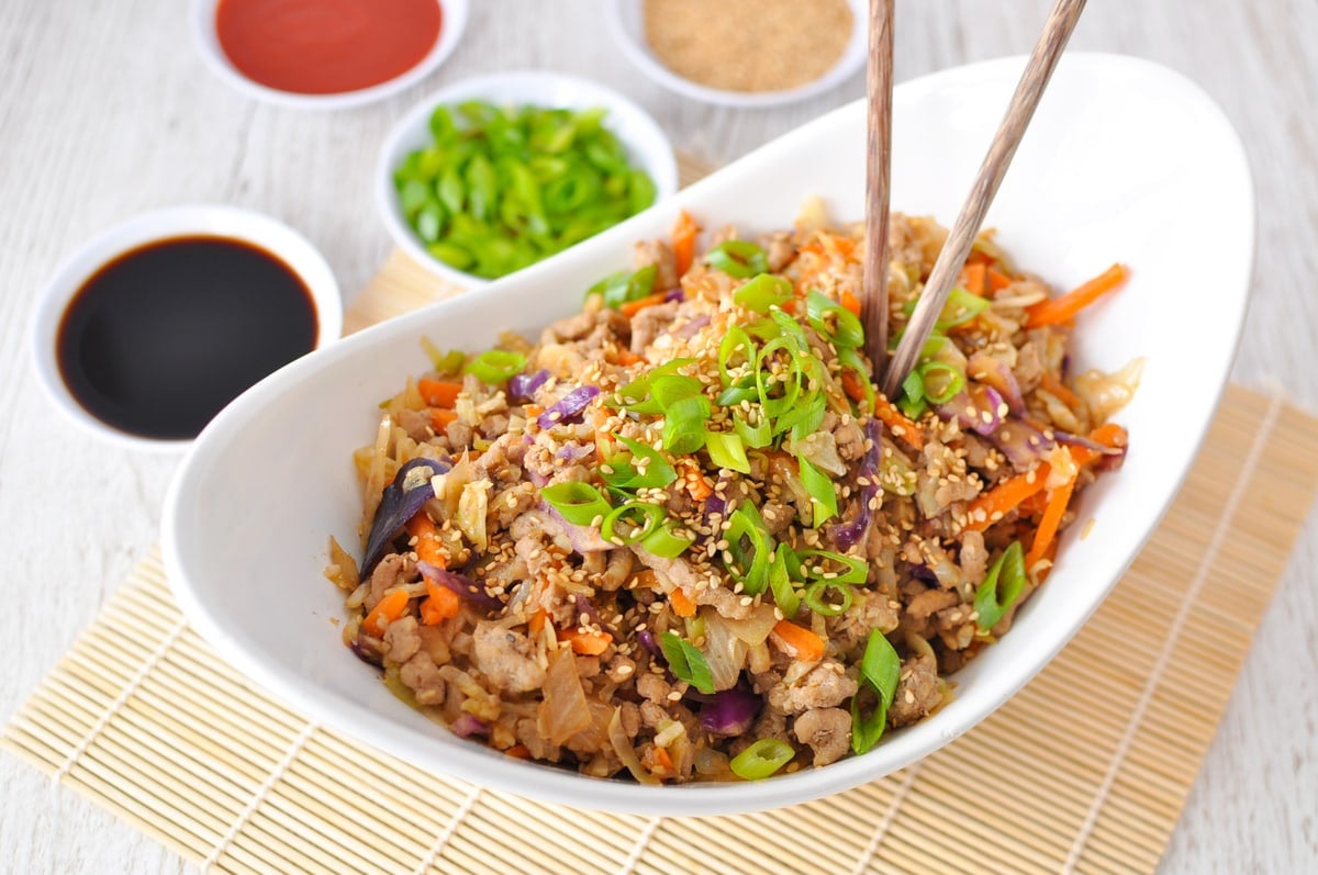 Egg roll in a bowl in a white serving dish with chopsticks, garnished with green onions