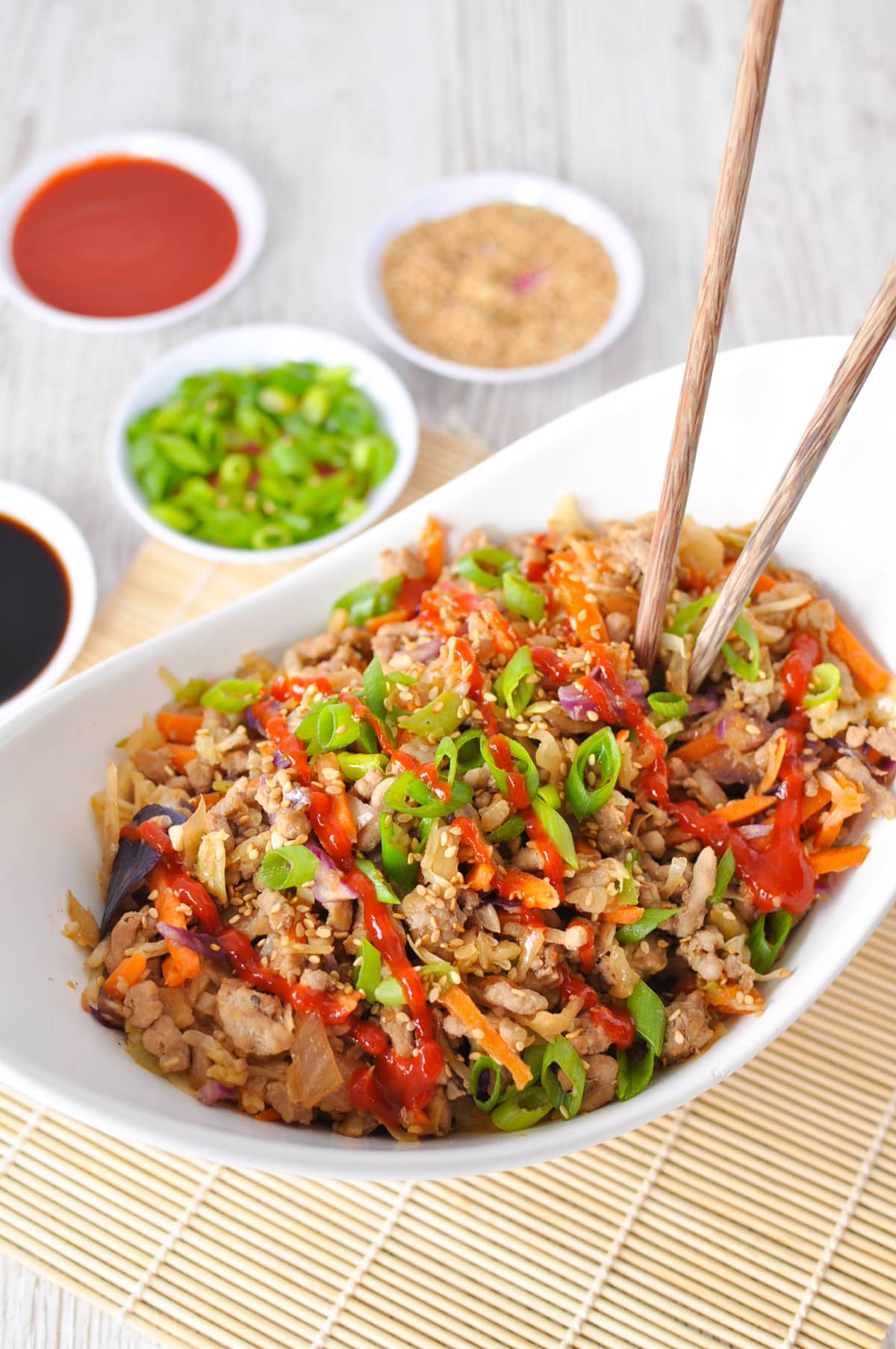 A white serving dish filled with egg roll in a bowl, garnished with green onions and sriracha