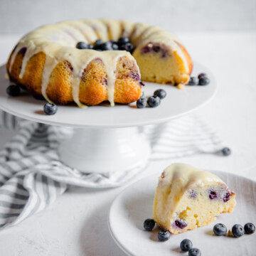 keto blueberry lemon pound cake on a cake stand, with a glazed slice in front of it