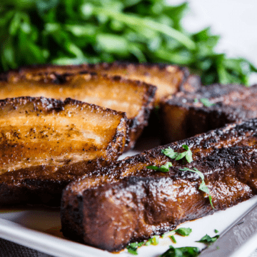 Coffee Barbecue Pork Belly, sliced and fried till crispy, served on a white square plate with fresh herbs.