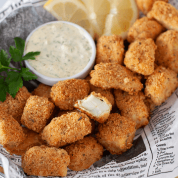 a wire basket lined with parchment paper, filled with crispy fish nuggets, tartar and lemon