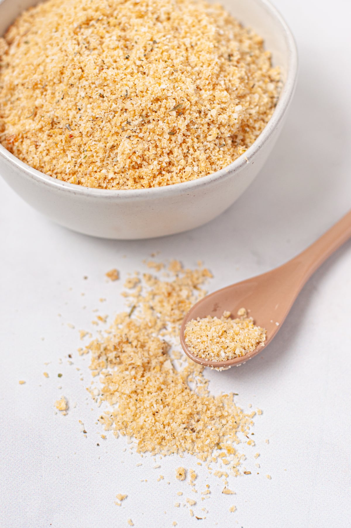 a small white bowl with gluten free breading and a spoon with breading spilling out of it