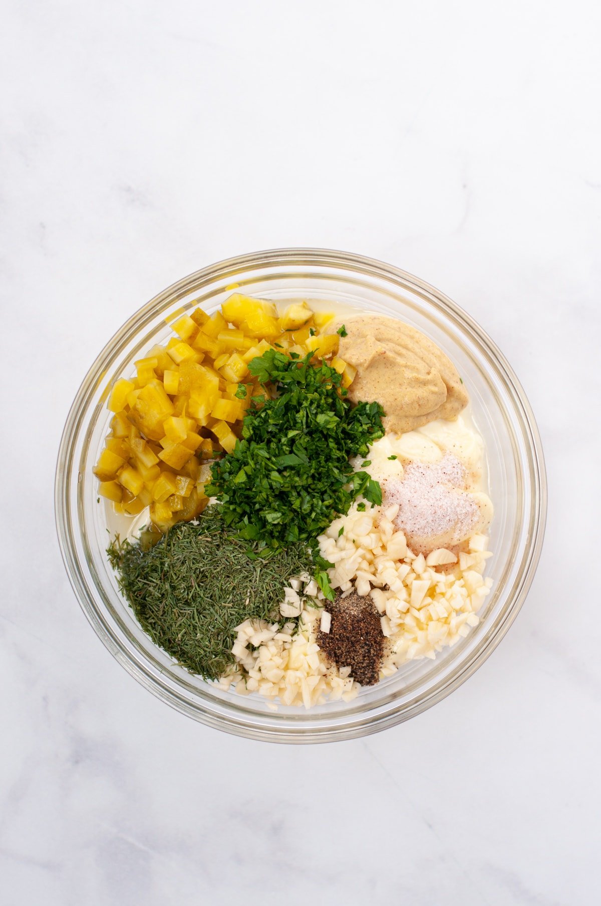 A mixing bowl with mayonnaise, dijon, pickles, garlic, dill, parsley, salt and pepper