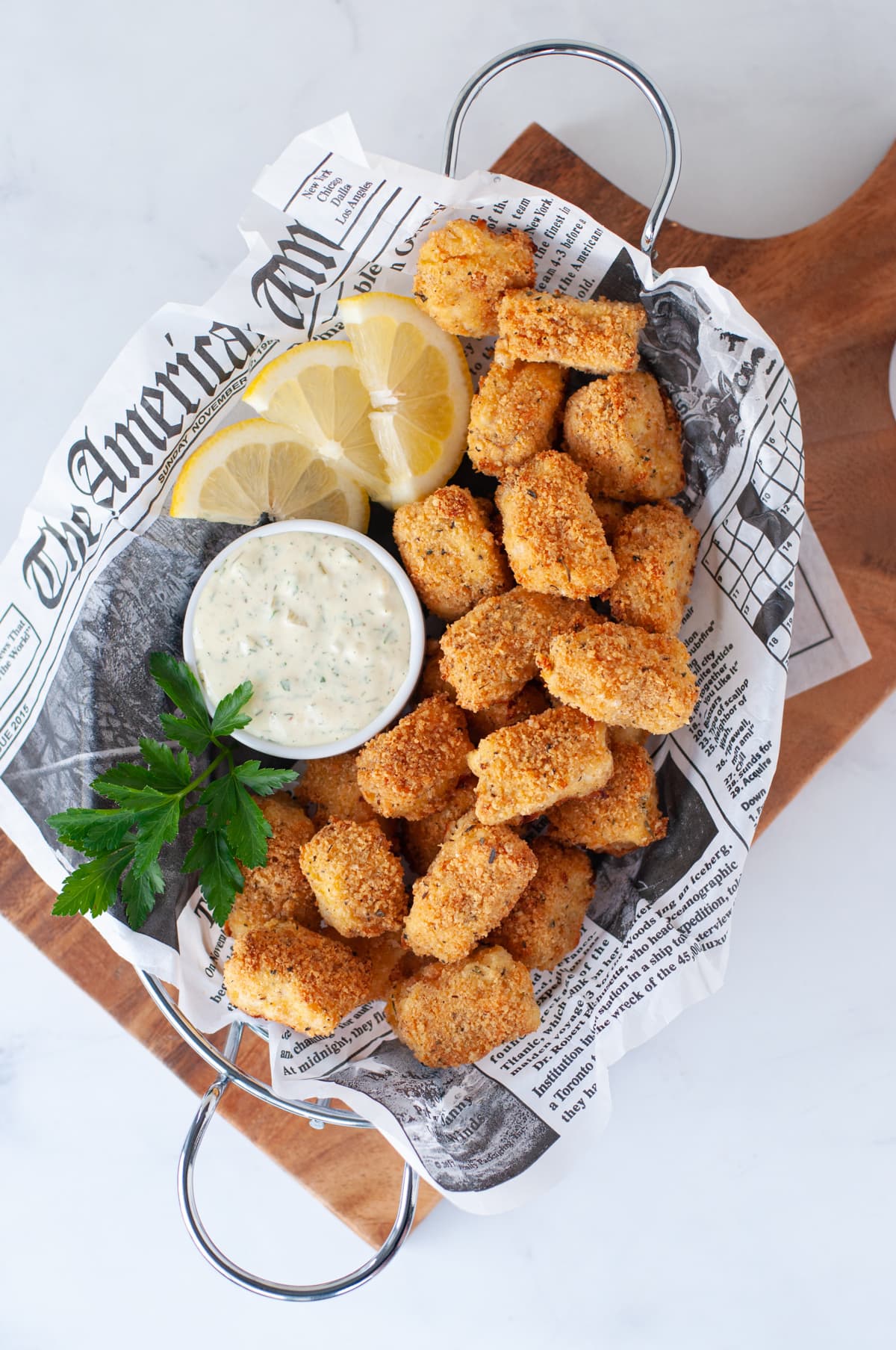 a wire basket lined with parchment paper, filled with keto fish sticks, tartar and lemon