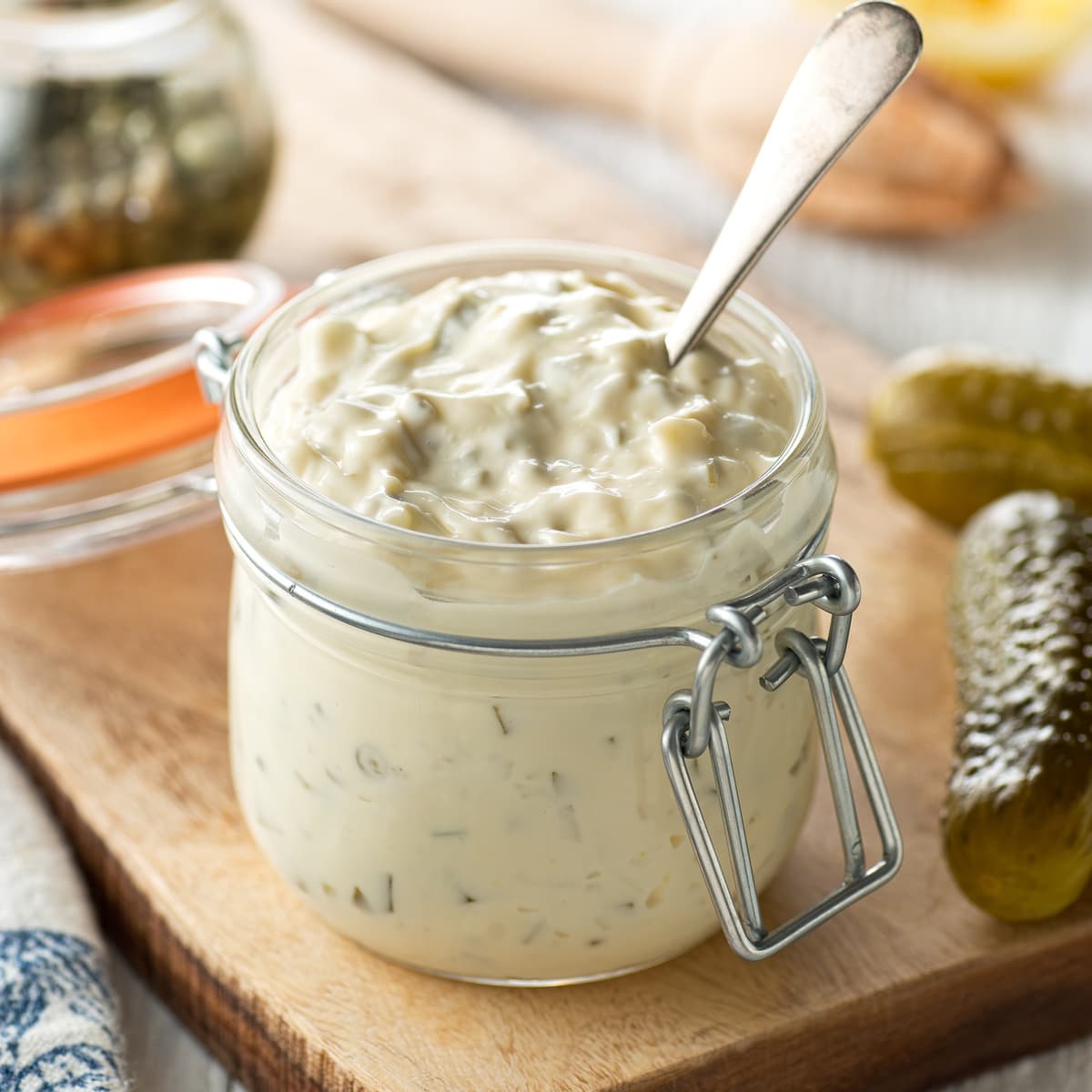 a jar of homemade tartar sauce, surrounded by pickles, and lemons