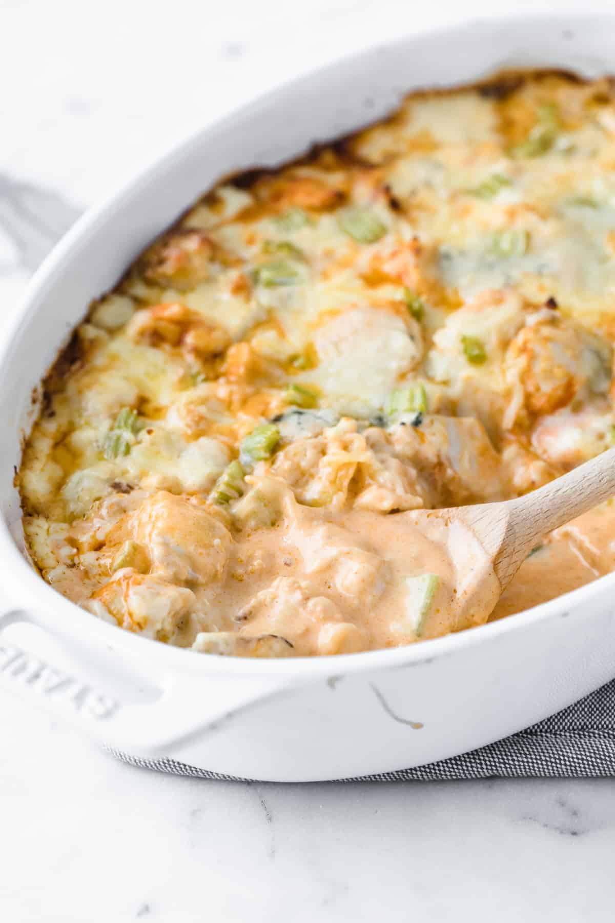 white casserole dish with low carb buffalo chicken Mac and cheese, with a wood serving spoon