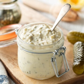 a jar of homemade tartar sauce, surrounded by pickles, and lemons