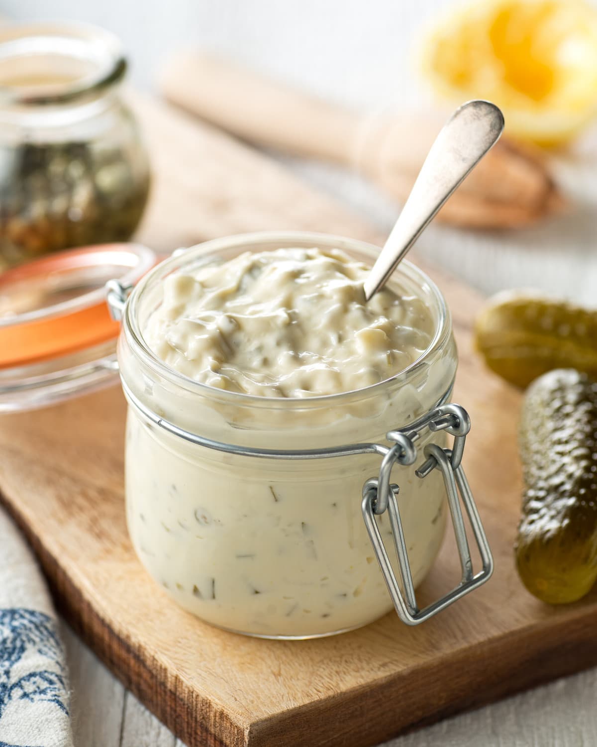 a jar of homemade tartar sauce, surrounded by pickles, and lemons