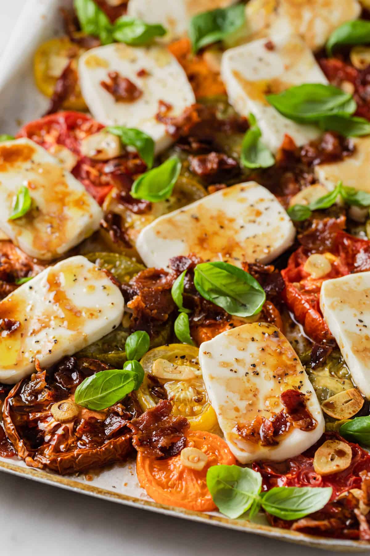 baking sheet with baked caprese salad - heirloom tomatoes, basil, fresh mozzarella, bacon, garlic, olive oil 