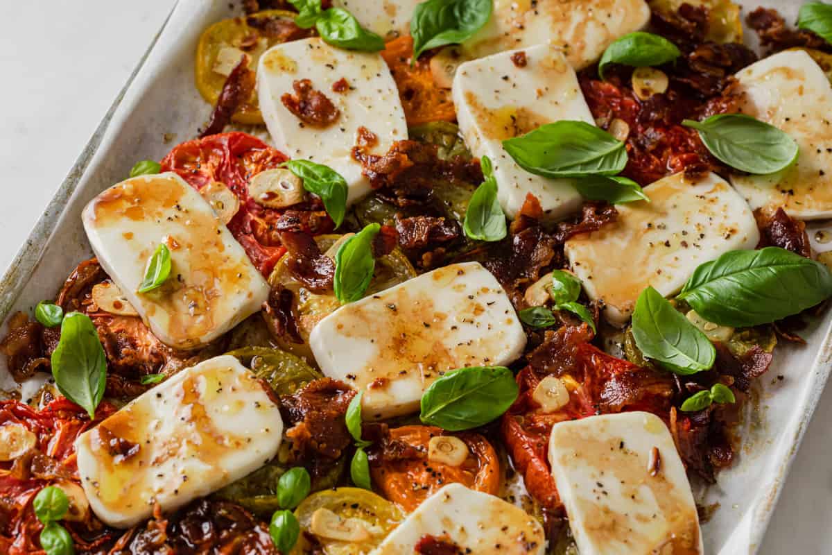 baking sheet with baked caprese salad - heirloom tomatoes, basil, fresh mozzarella, bacon, garlic, olive oil 