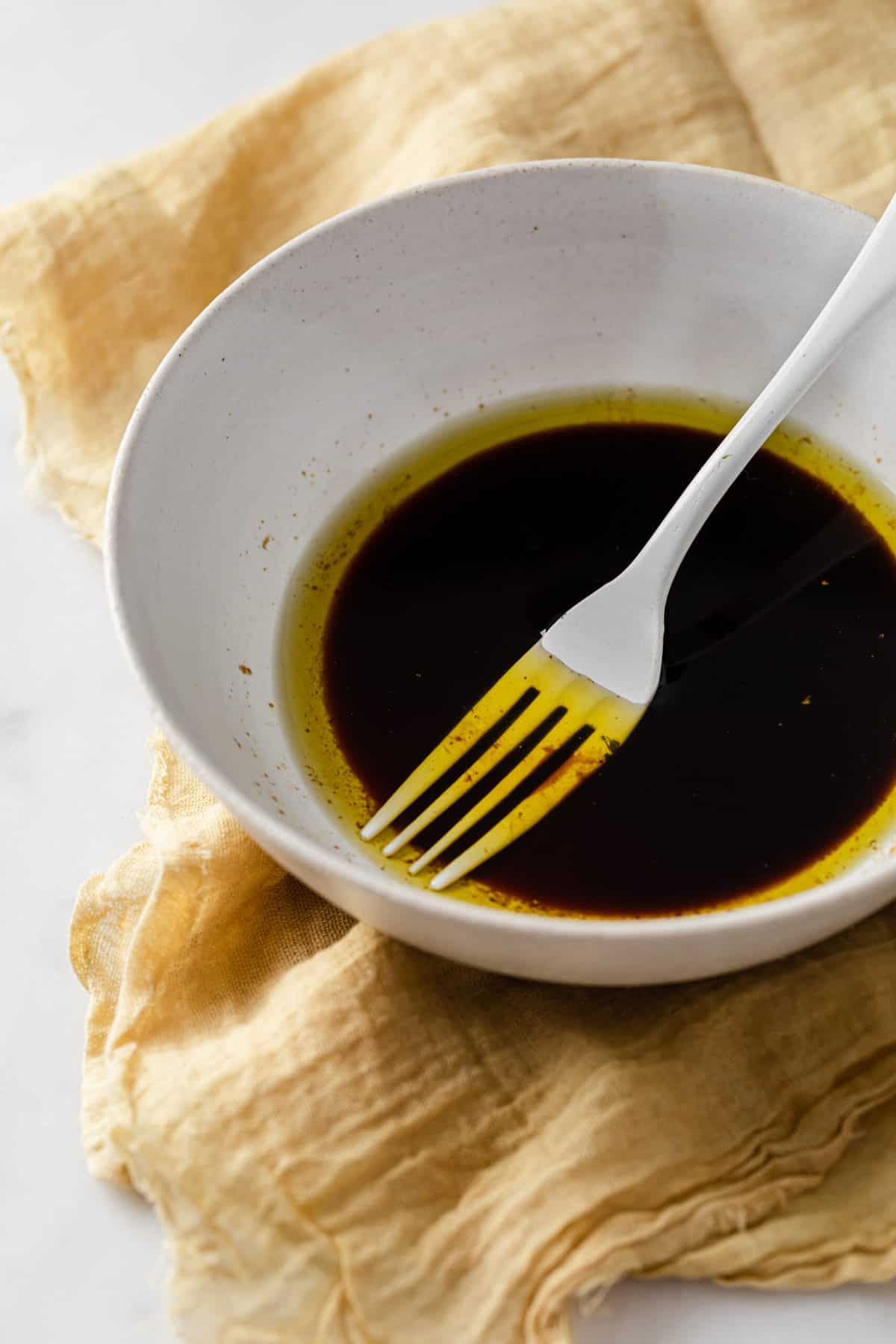 White bowl with balsamic vinegar, bacon drippings and olive oil, with a fork to whisk 