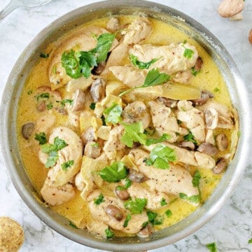 skillet with chicken tenders in a creamy mustard sauce, with mushrooms, artichokes, and fresh parsley