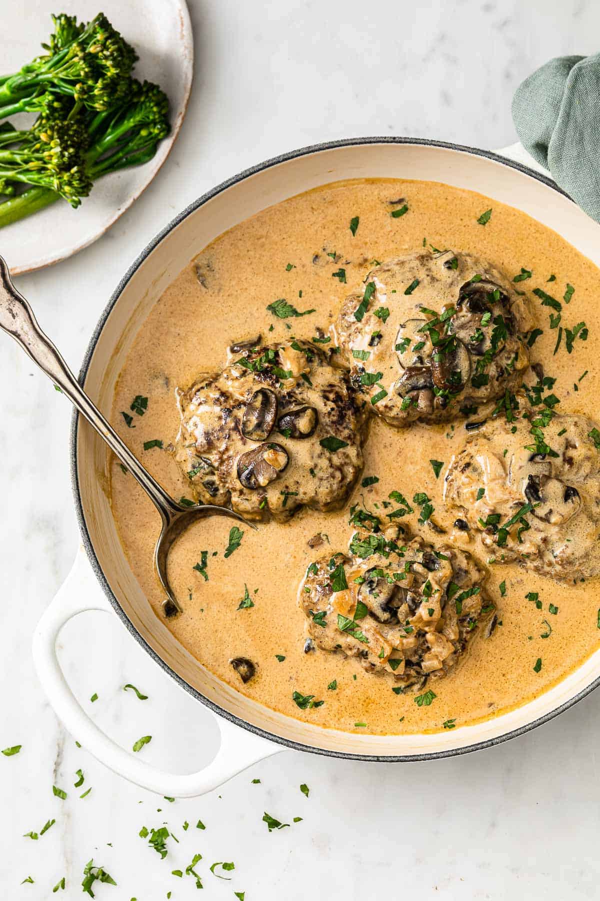 beef patties in a skillet, with stroganoff sauce, mushrooms, and onions, garnished with parsley
