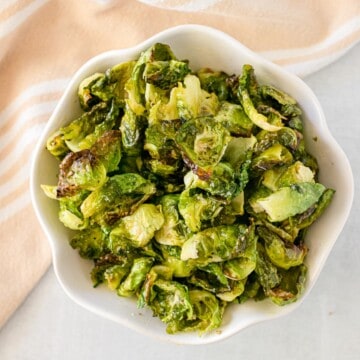 white bowl full of crispy Brussels sprouts chips, with fresh Brussels sprouts in the background
