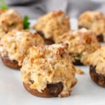 Sausage stuffed mushrooms on a white plate, garnishes with parsley.