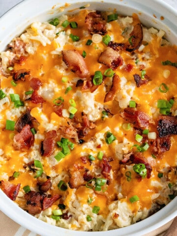 white casserole dish with a twice baked cauliflower with bacon, cheese, and green onions.