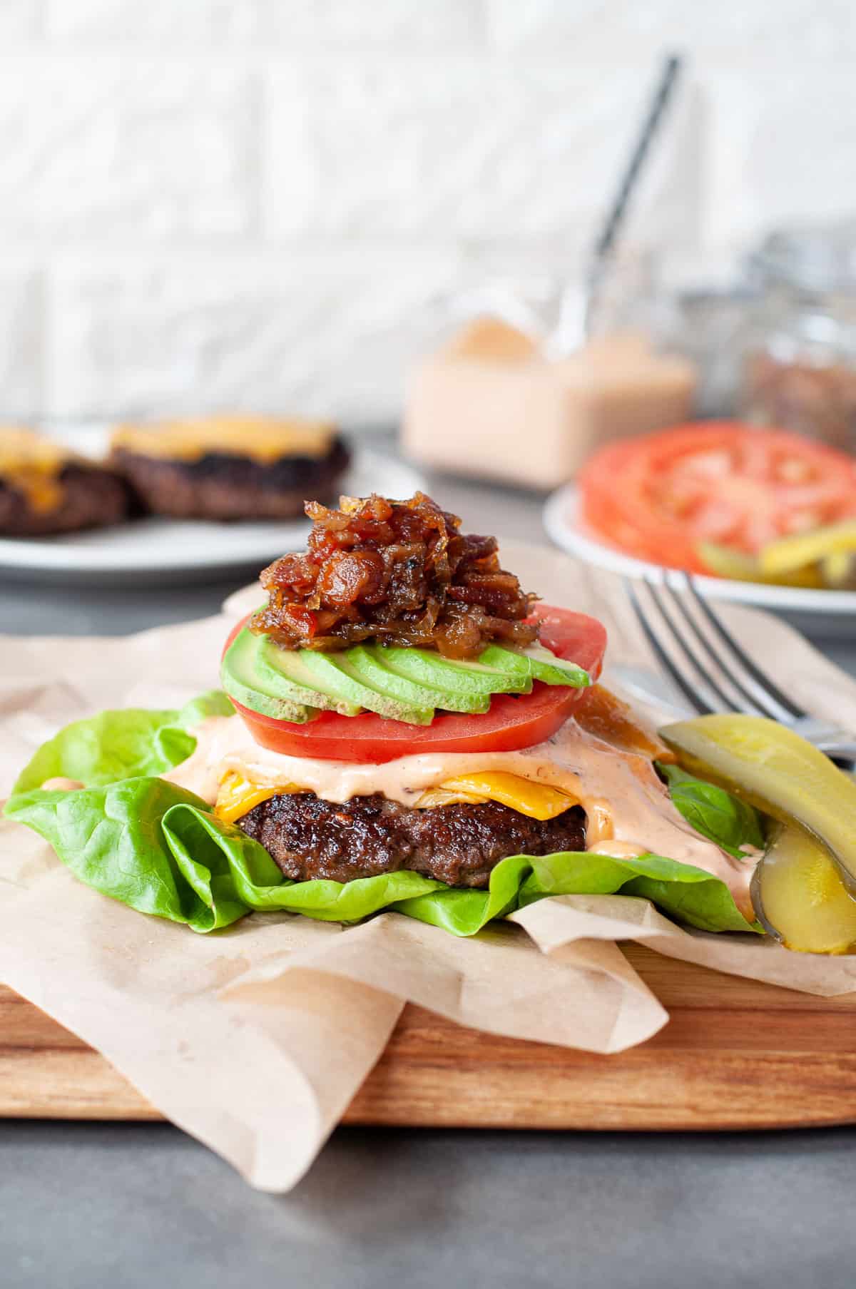 Bunless burger on a bed of lettuce, topped with cheese, sauce, tomato, avocado and bacon jam