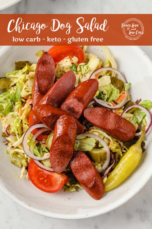 a salad piled high with grilled hot dogs, pickles, red onion, peppers, tomatoes, and a mustard dressing