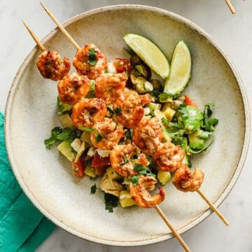 grilled prawns on top of an avocado feta salsa, plated with lime wedges.