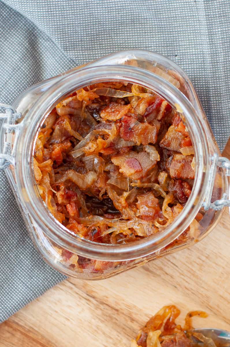 a jar full of keto bacon jam, on a wooden pizza peel, with a serving spoon