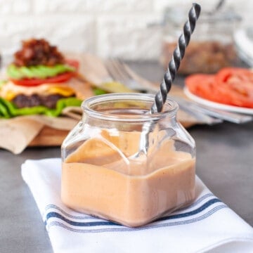 a jar of burger sauce with a burger, and bacon jam in the background