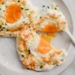 2 baked egg clouds, topped with chives, on a white ceramic plate with a fork.