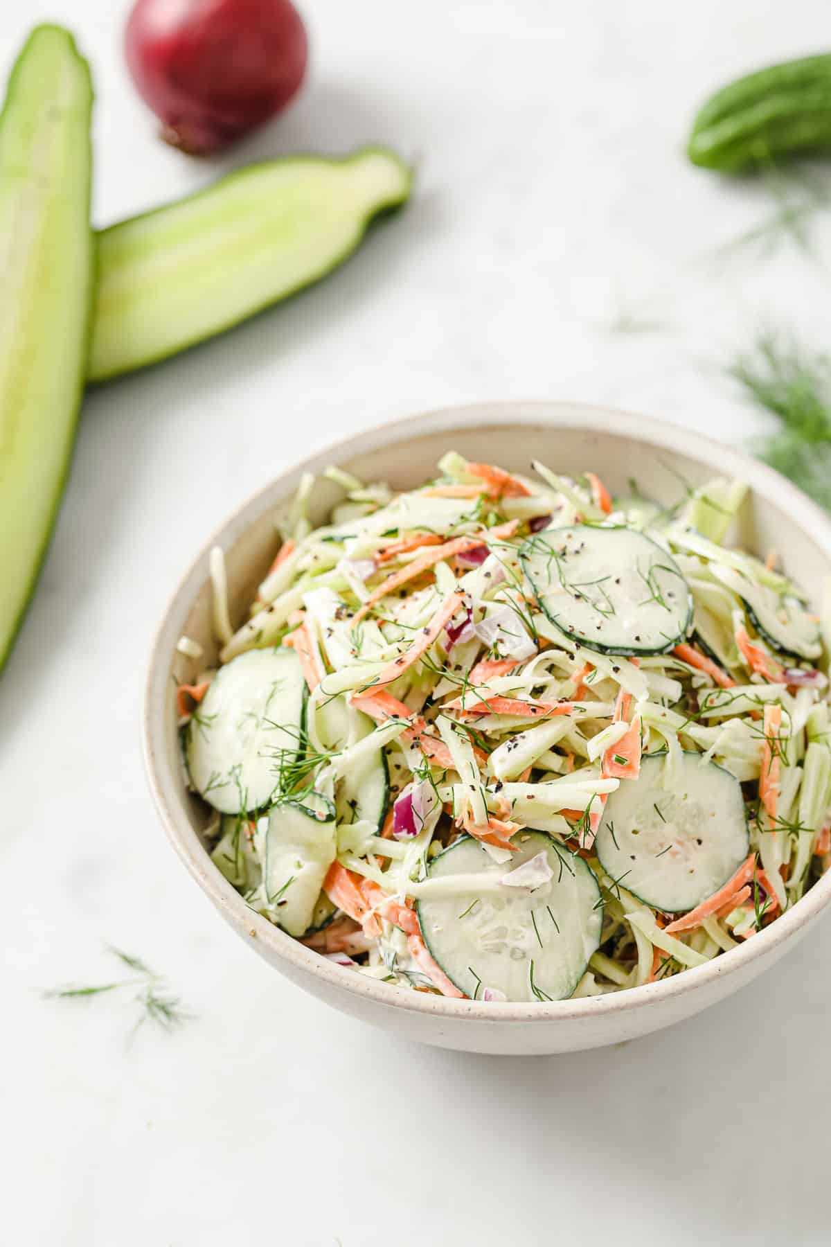 a bowl of paleo coleslaw with broccoli slaw, cucumber, mayo, red onion, dill, garlic, salt and pepper
