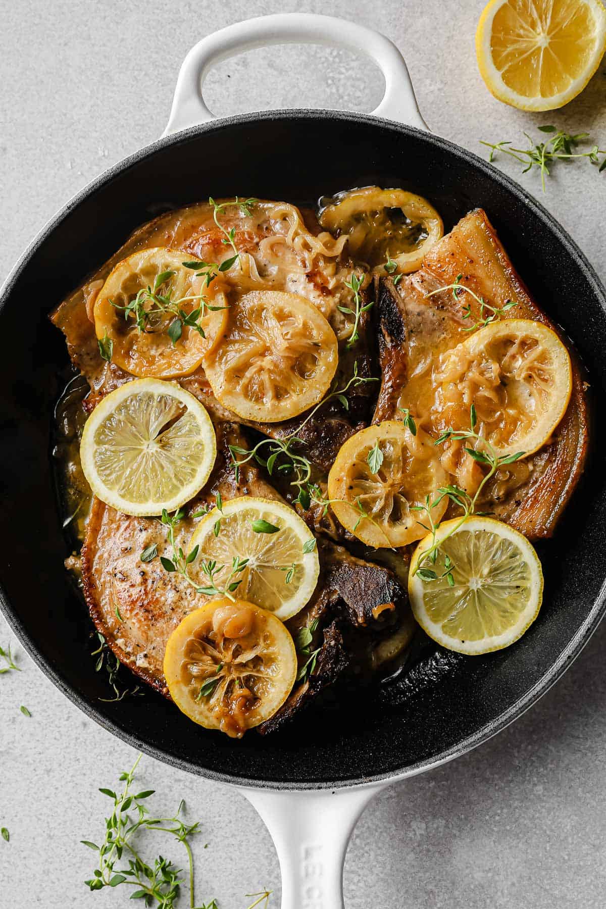 cast iron skillet with pork chops, fresh lemons, thyme, and pan sauce