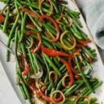 a white plate full of an asian inspired green bean dish - green beans, onion, peppers, soy sauce, butter, brown sugar
