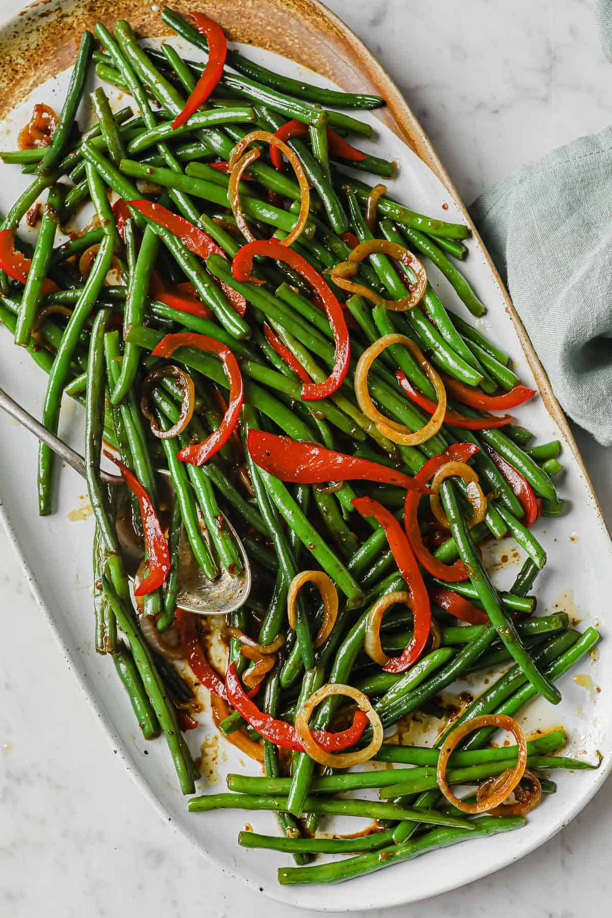 a white plate full of an asian inspired green bean dish - green beans, onion, peppers, soy sauce, butter, brown sugar