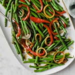 a white plate full of an asian inspired green bean dish - green beans, onion, peppers, soy sauce, butter, brown sugar.
