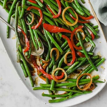 a white plate full of an asian inspired green bean dish - green beans, onion, peppers, soy sauce, butter, brown sugar.