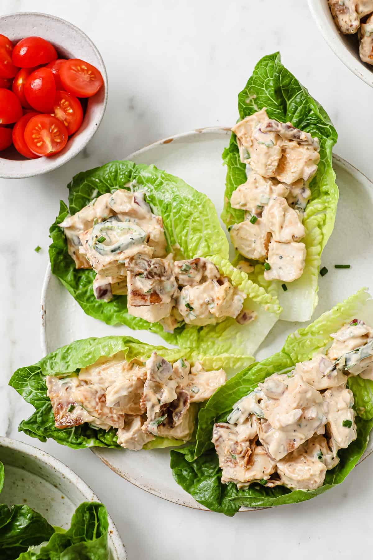 a bowl of chicken salad, surrounded by fresh tomatoes, chives, and lettuce wraps