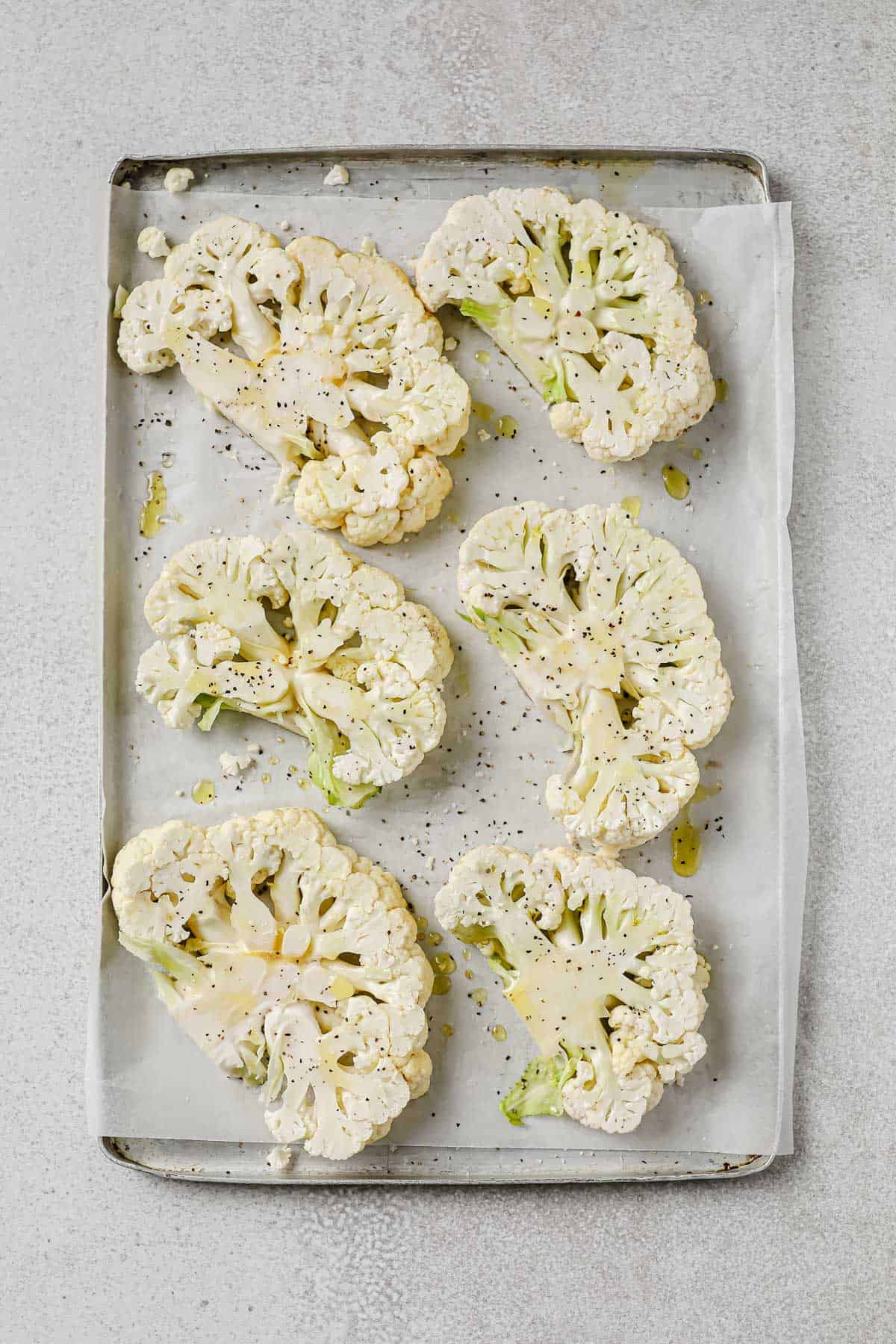 Cauliflower sliced into steaks and spread on a baking sheet, seasoned with olive oil, salt and pepper