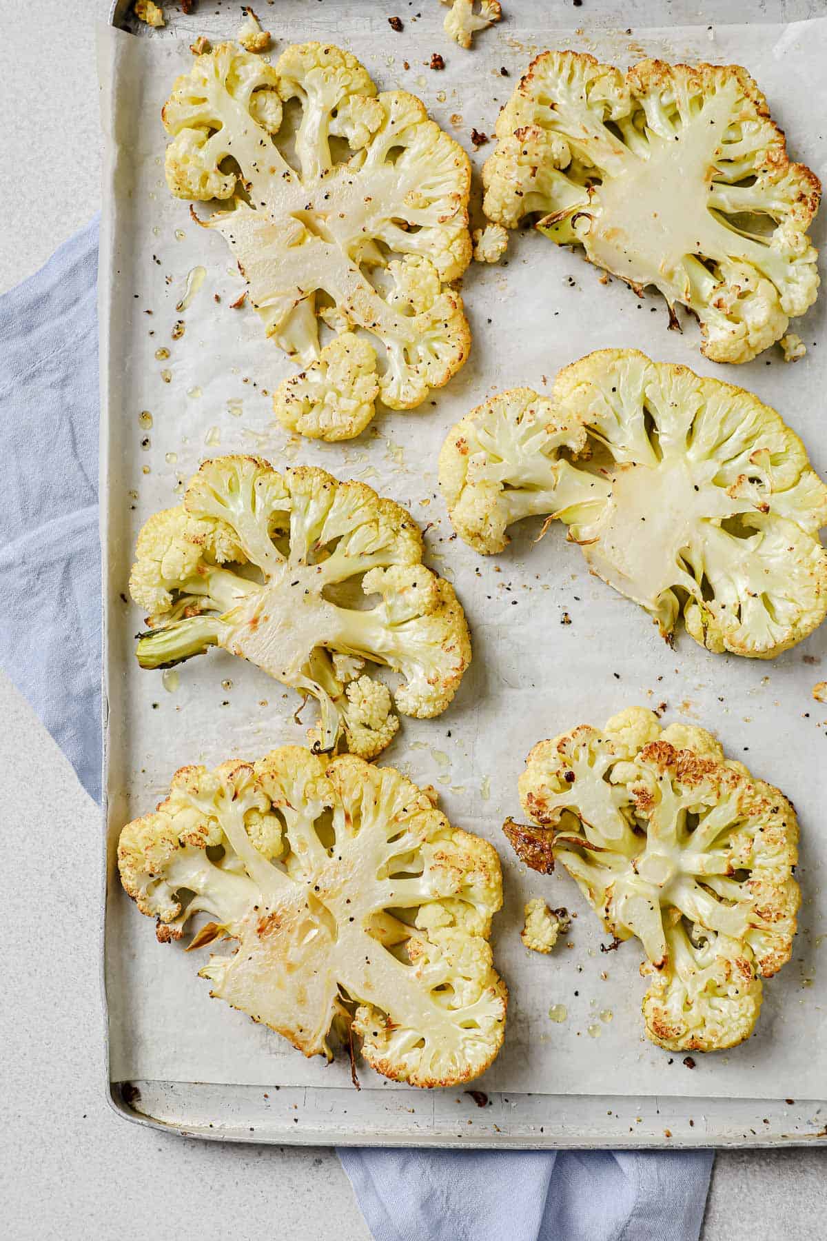Roasted cauliflower steaks on a lined baking sheet, seasoned with salt and pepper