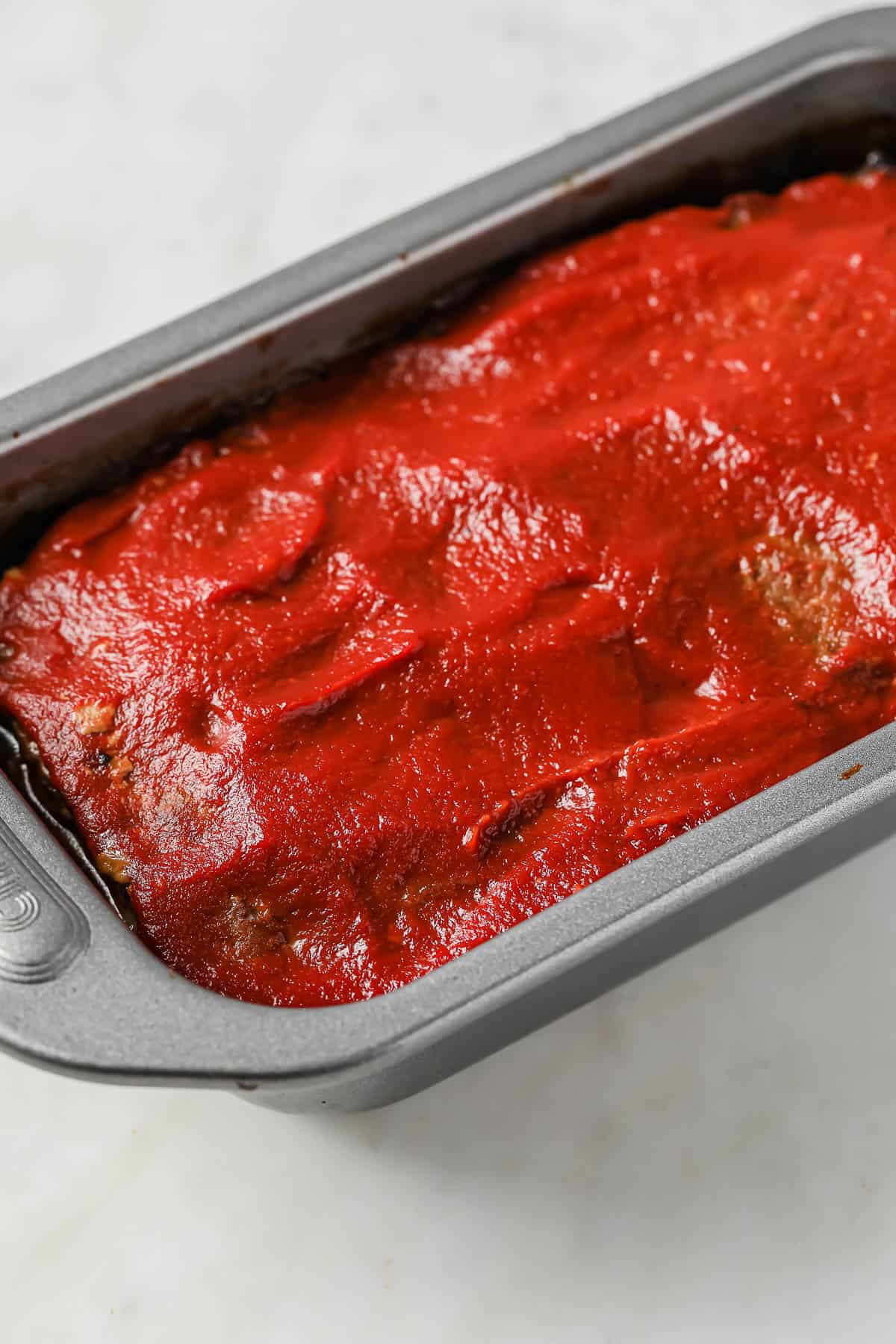 a loaf pan full of cooked meatloaf, topped with ketchup