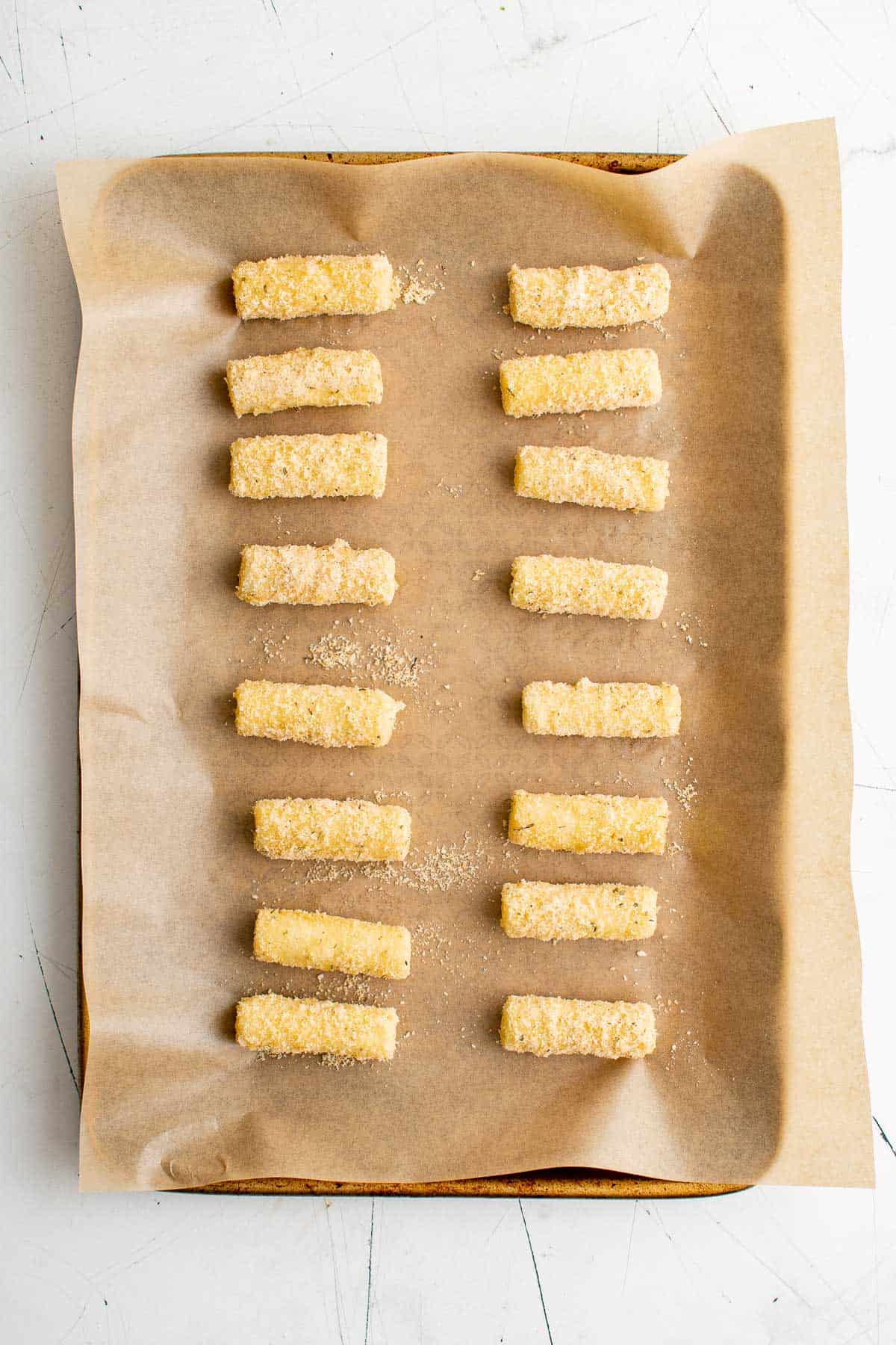 a parchment lined baking sheet, topped with rows of breaded mozzarella sticks waiting to be fried