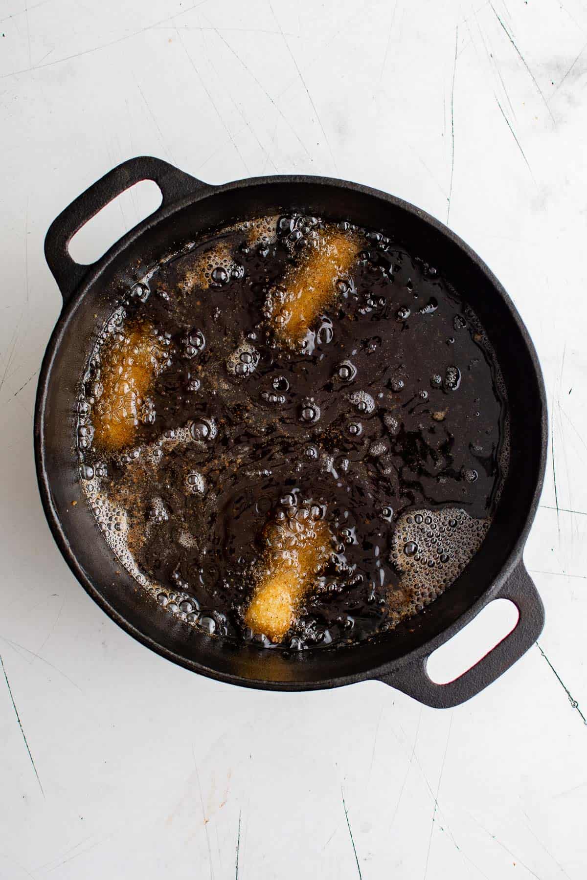 a cast iron pan with hot oil, frying cheese sticks