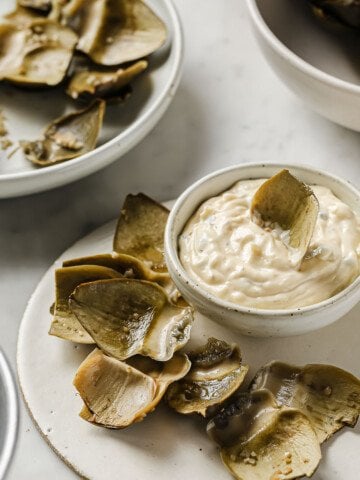 steamed artichokes with plucked leaves next to them, served with a lemon caper aioli sauce.