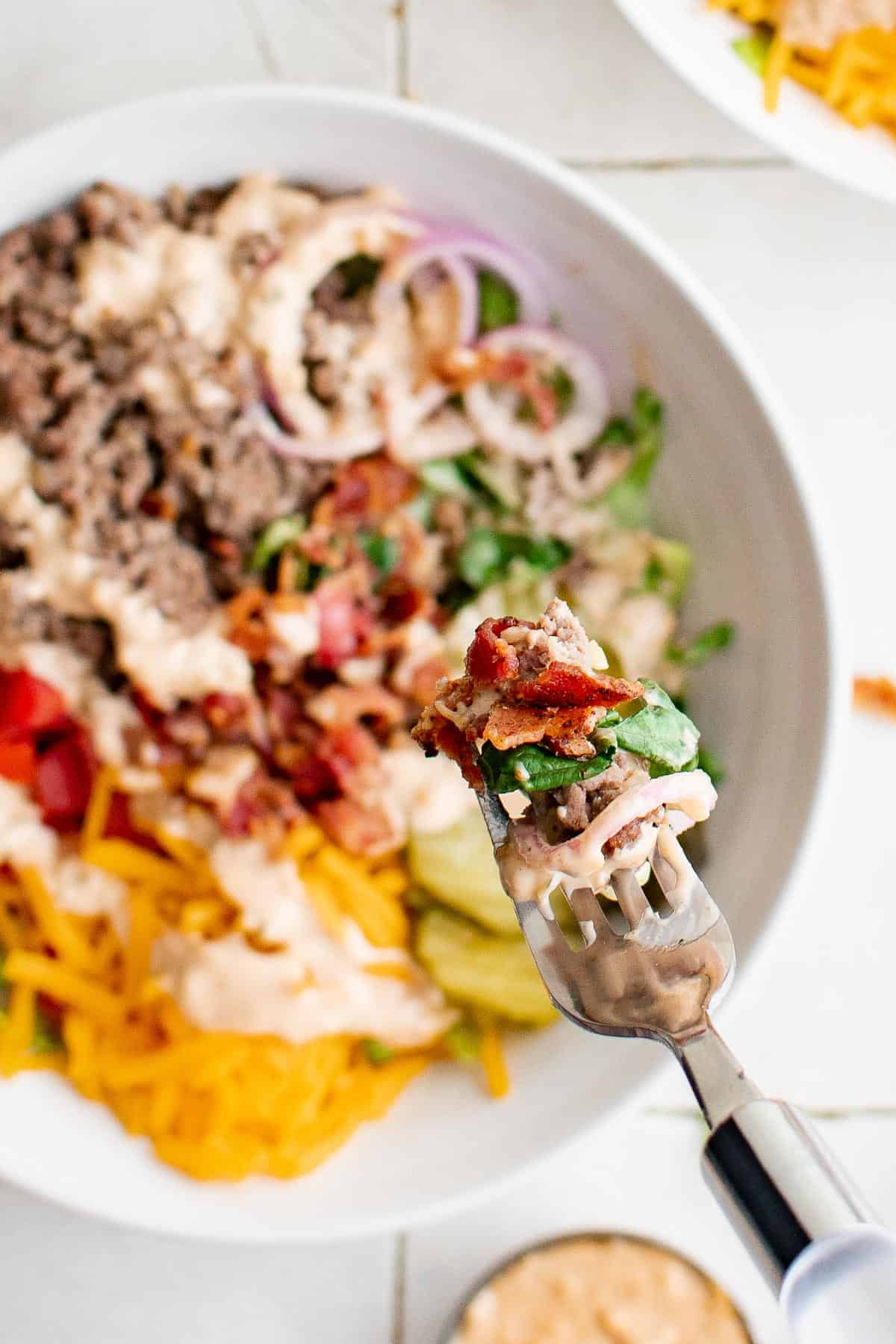 a salad made with ground beef, cheese, bacon, onion, tomatoes, pickles and burger sauce