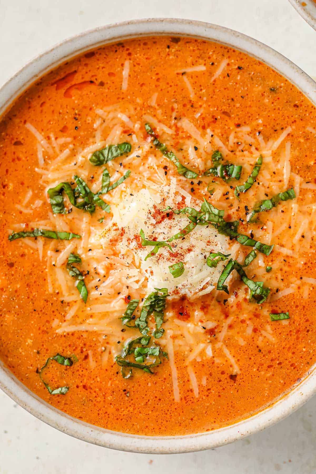 a bowl of lasagna soup, topped with ricotta cheese, parmesan cheese and fresh basil
